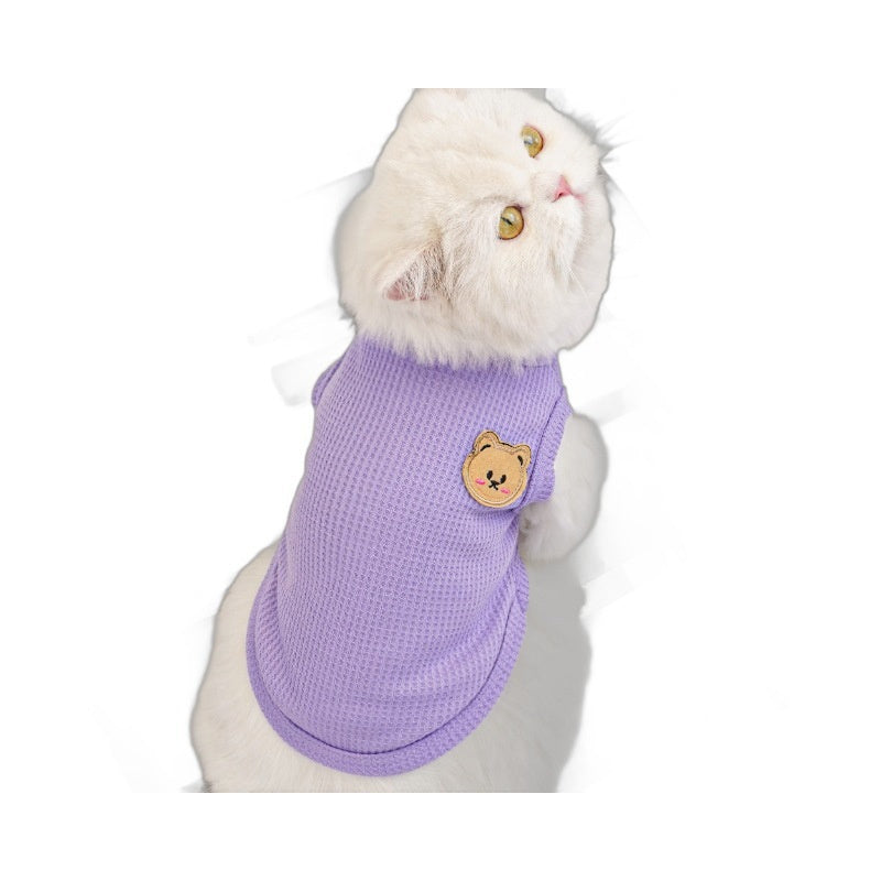 White cat model wearing a purple pet vest with a small bear patch, side view indoors
